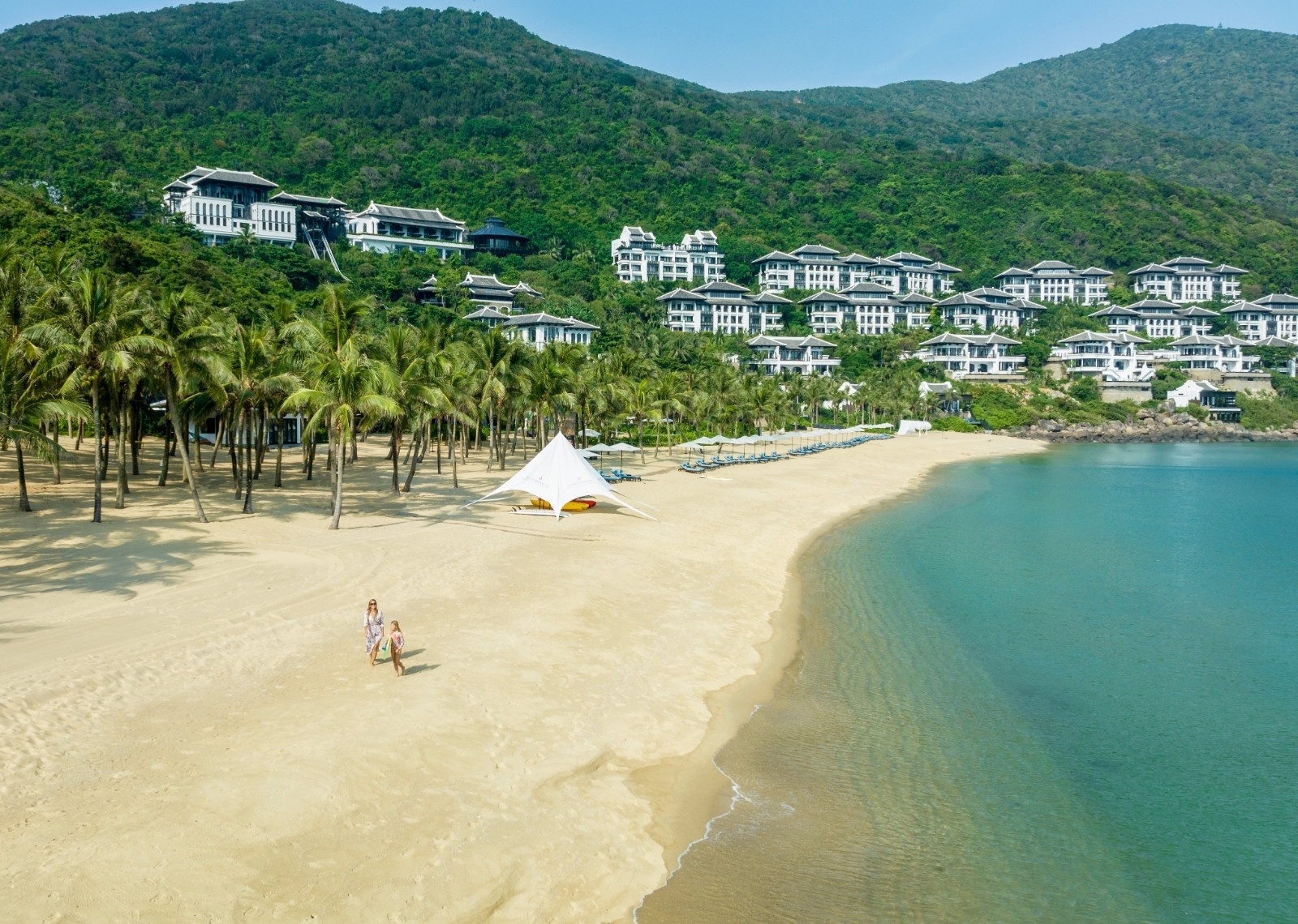 Aerial view of guests walking on a private white sand beach with luxury hillside villas at InterContinental Danang.