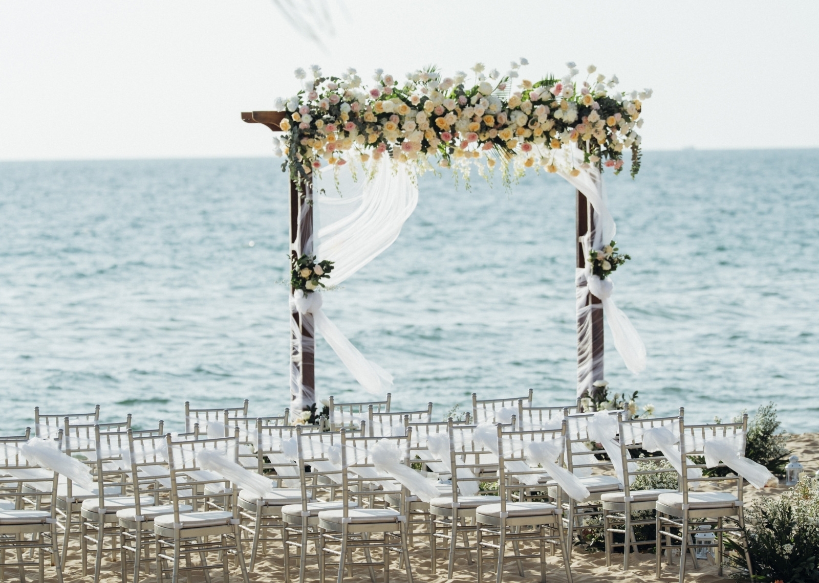 A wedding arch decked with flowers and voile in front of chairs set out for a beachside wedding at Wyndham Grand Phu Quoc.