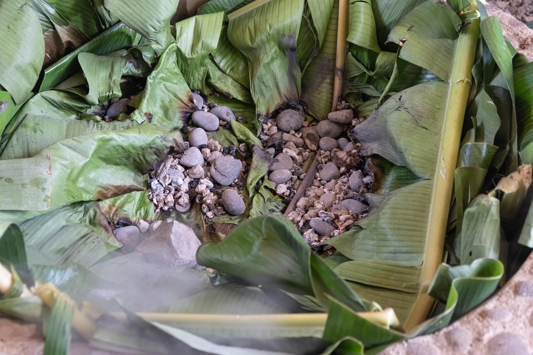 Hot stones and banana leaves being used for hāngī cooking.
